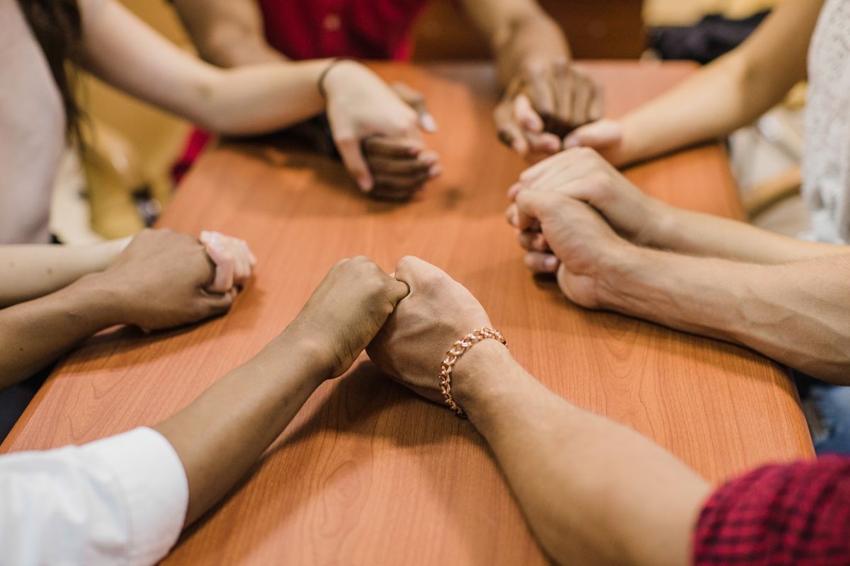 Top view of business people holding hands, leaning on wooden table, cropped